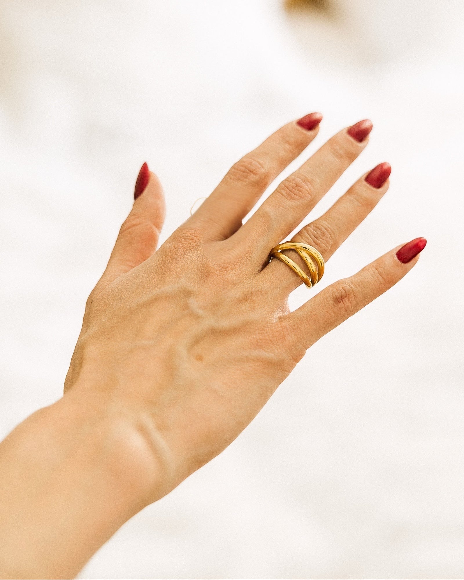 Gold-plated adjustable open-band ring worn on hand against white fabric
