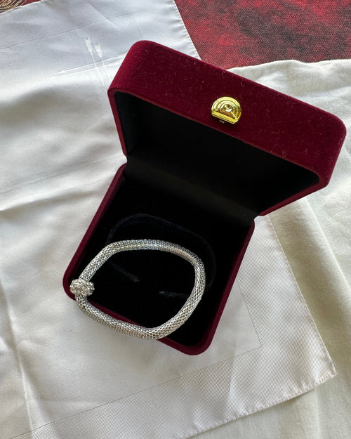 A silver-toned diamond-encrusted bracelet displayed inside an open dark red velvet jewelry box with a gold clasp, set on a white satin fabric.