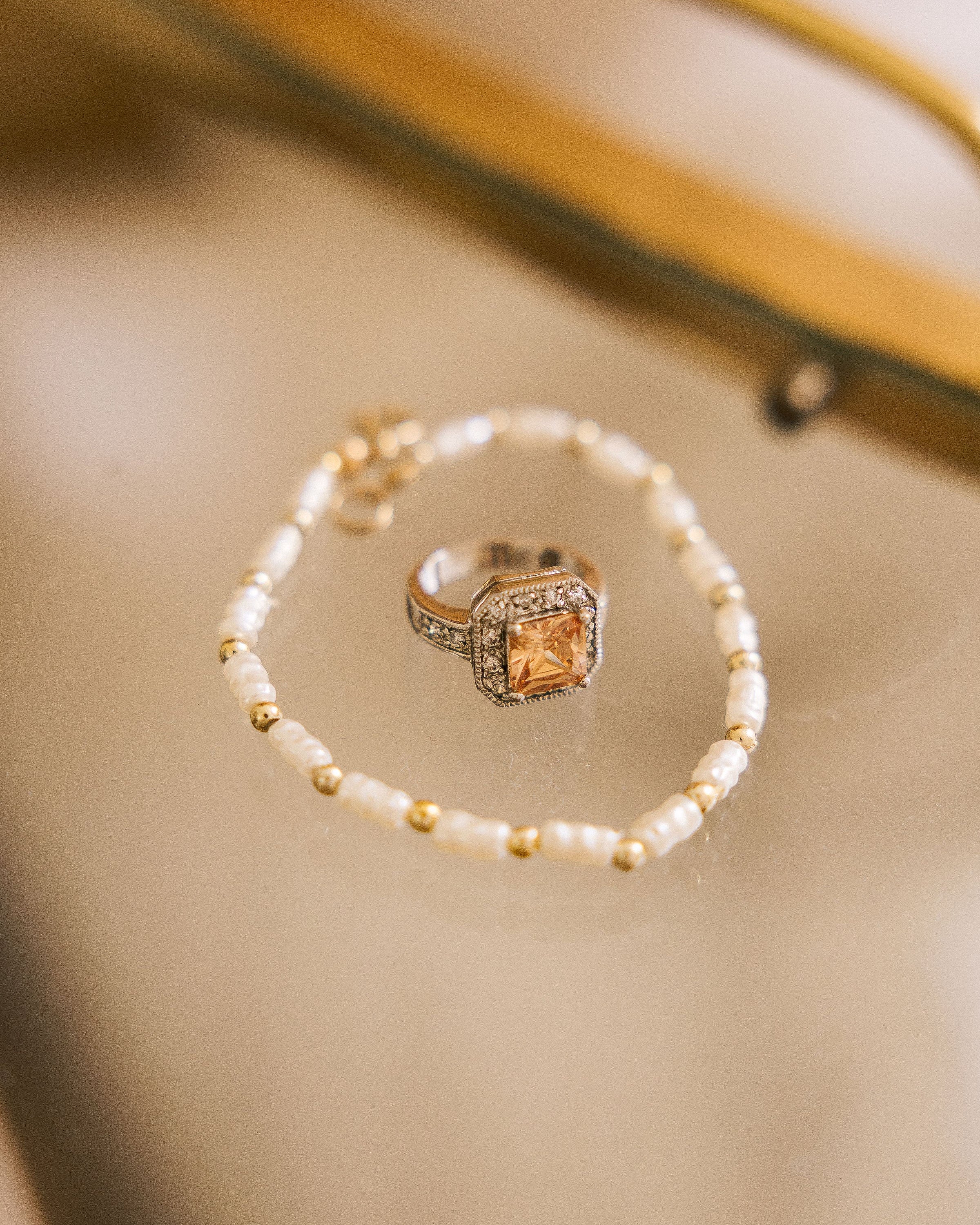 Bracelet with Pearl-Look Beads arranged around champagne statement ring on beige surface
