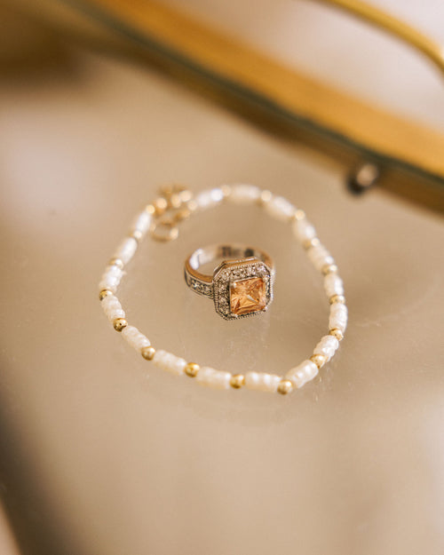 Bracelet with Pearl-Look Beads arranged around champagne statement ring on beige surface