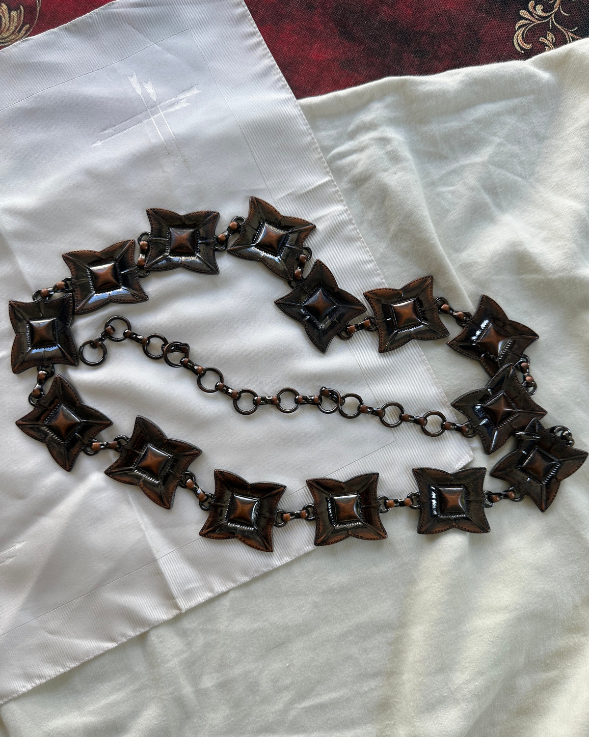 A dark bronze-toned chain necklace with repeating starburst-shaped links, laid out on a white fabric surface.