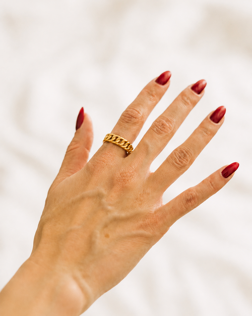 Gold-plated chain ring worn on hand against white fabric