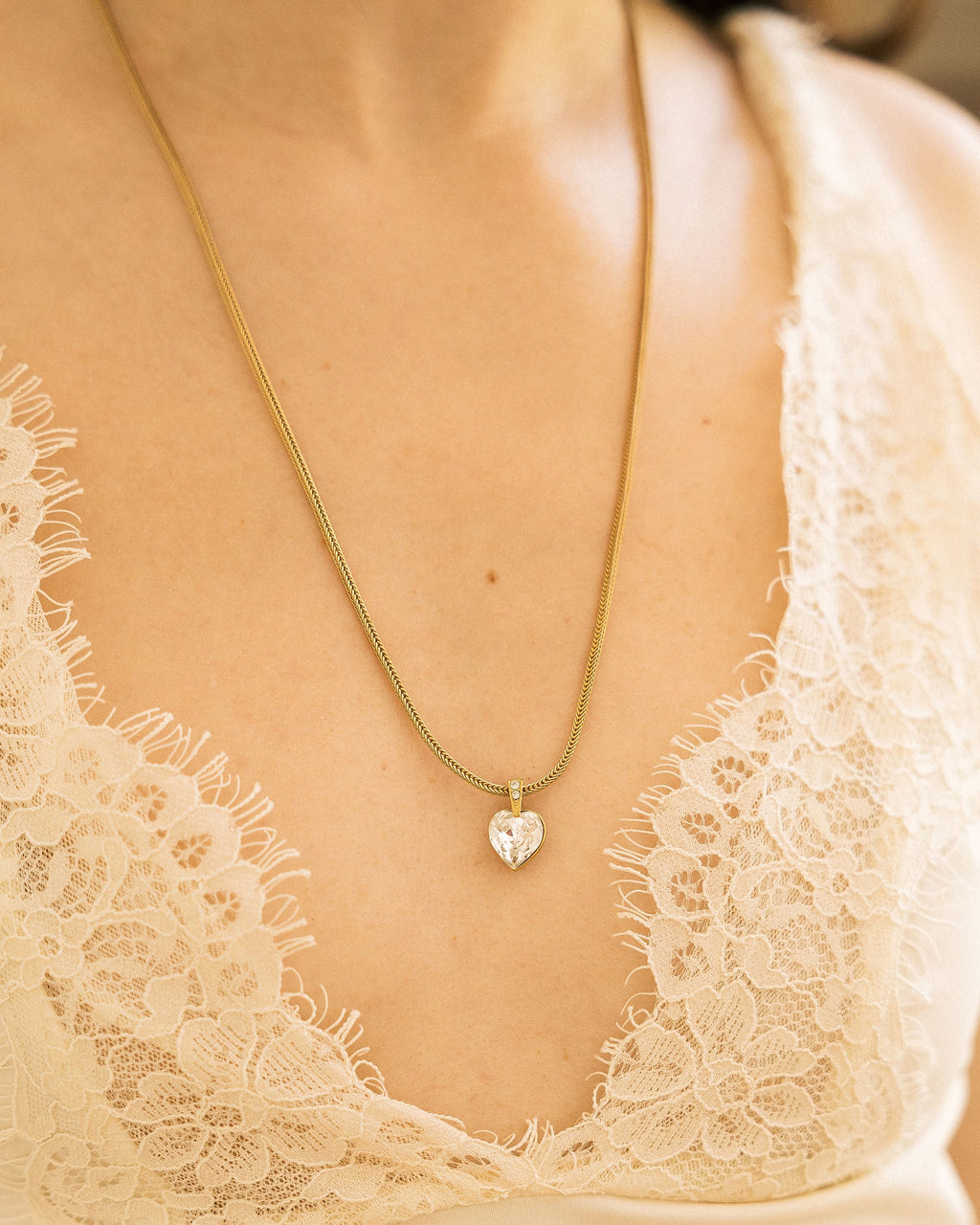 Crystal Heart Necklace hanging from vintage wooden cabinet with pink peonies