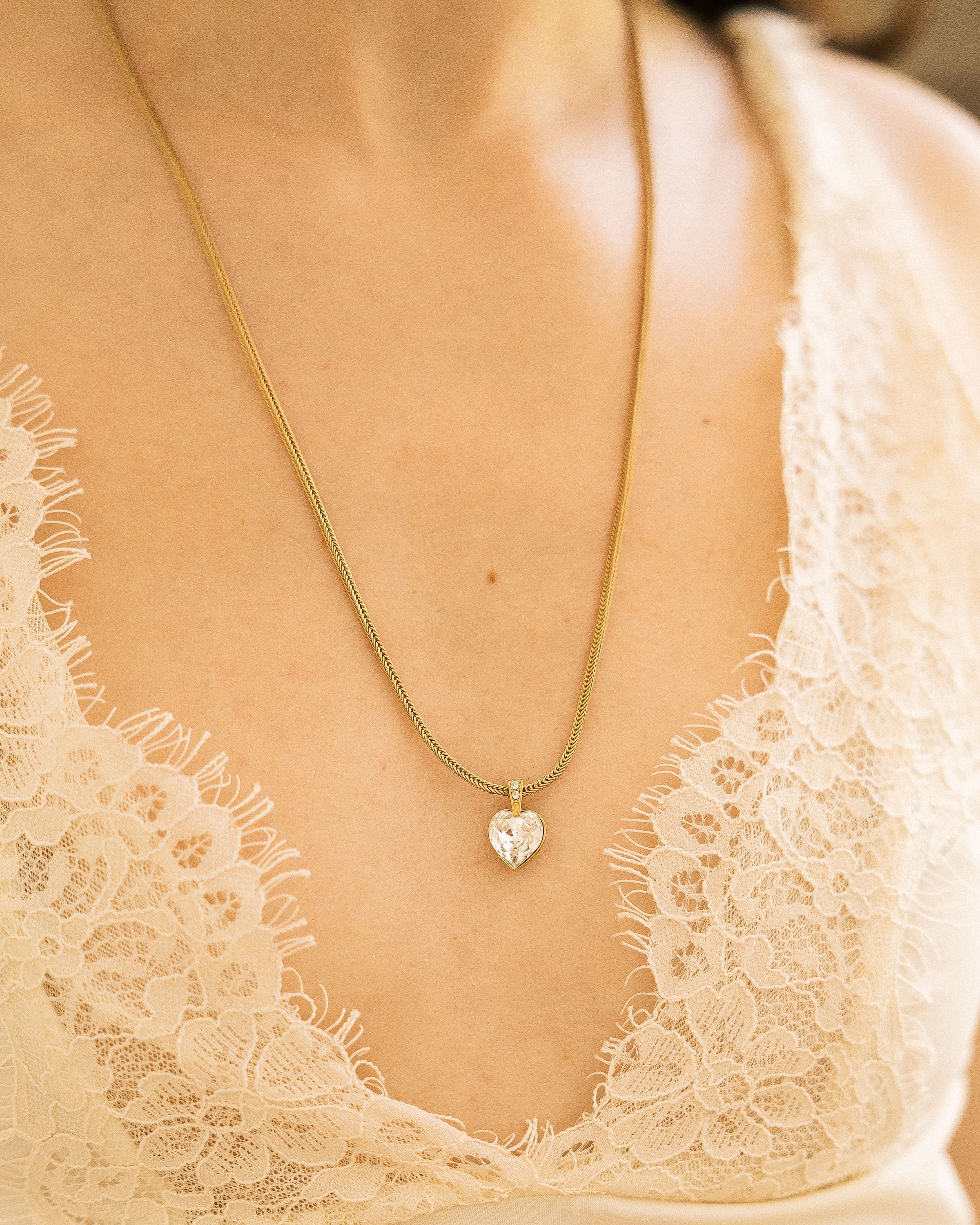 Crystal Heart Necklace hanging from vintage wooden cabinet with pink peonies
