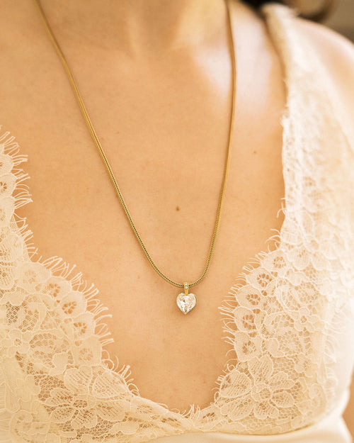 Crystal Heart Necklace hanging from vintage wooden cabinet with pink peonies