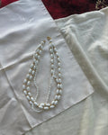 A white beaded necklace with gold-toned spacer details and a gold clasp, laid flat on a white satin fabric.