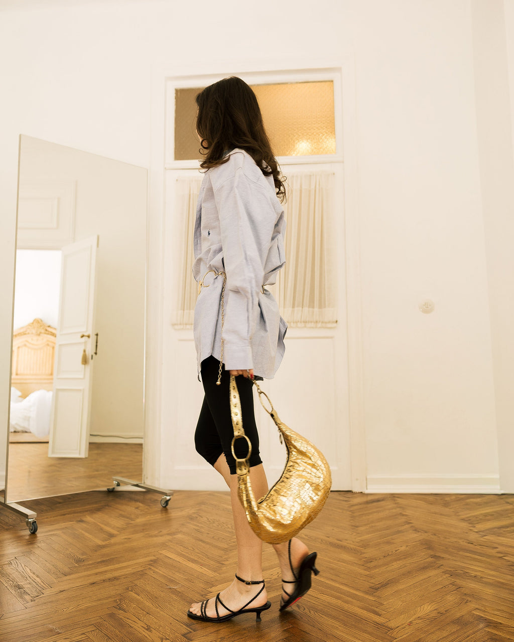 Gold Metallic Crescent Bag worn on shoulder by model in white top in doorway
