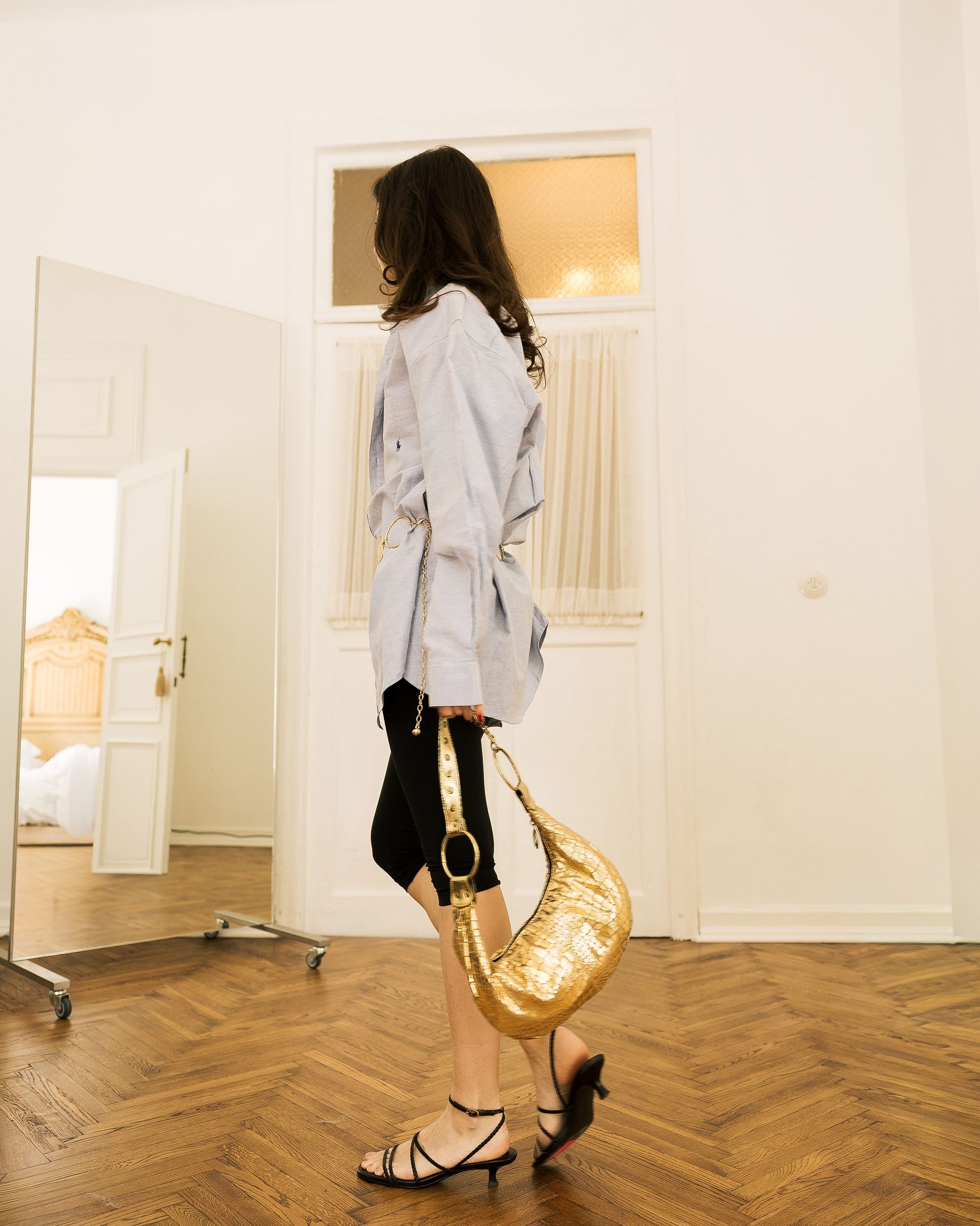 Gold Metallic Crescent Bag worn on shoulder by model in white top in doorway