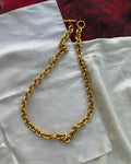 A chunky gold chain necklace with a toggle clasp, laid out on a white fabric surface with a red textured fabric in the background.