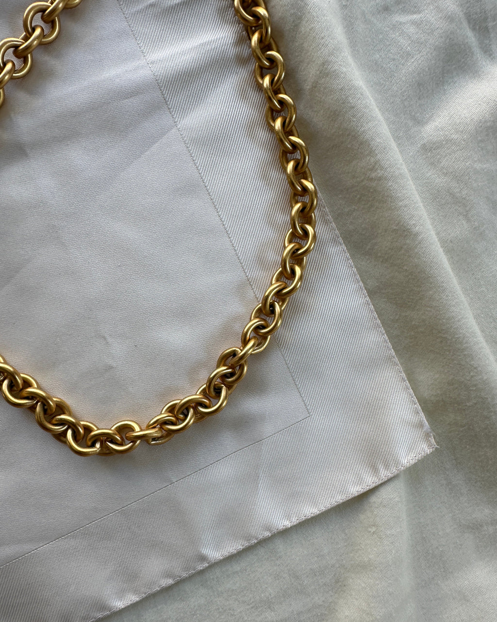 A close-up of a chunky gold chain necklace draped over a white fabric background.