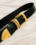 A close-up of a black textured leather belt with a gold buckle, resting on a white fabric background.