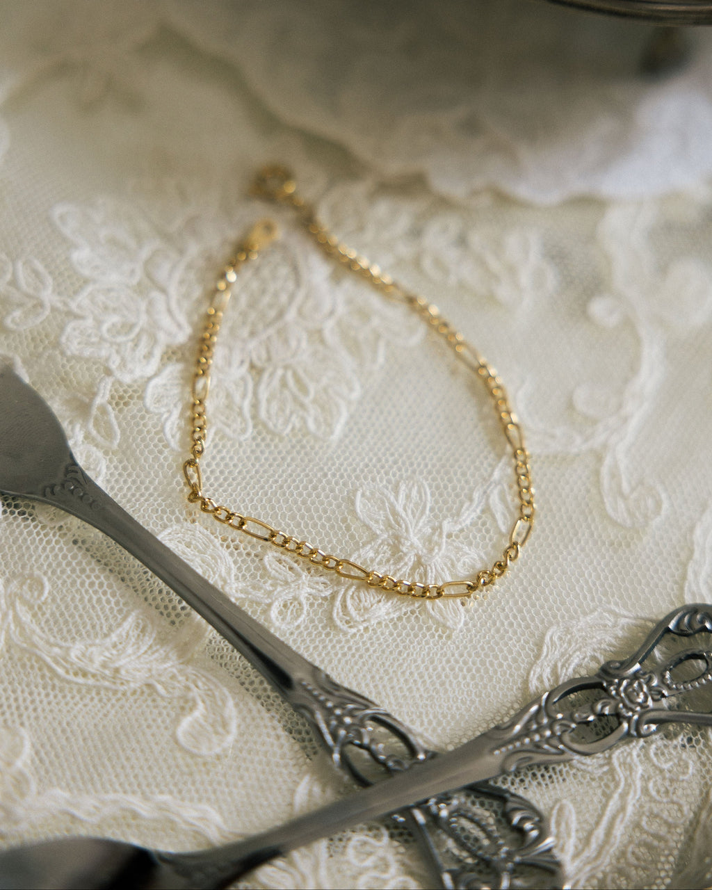 Minimalist Gold Chain Bracelet flat lay on white lace cloth with vintage silver scissors