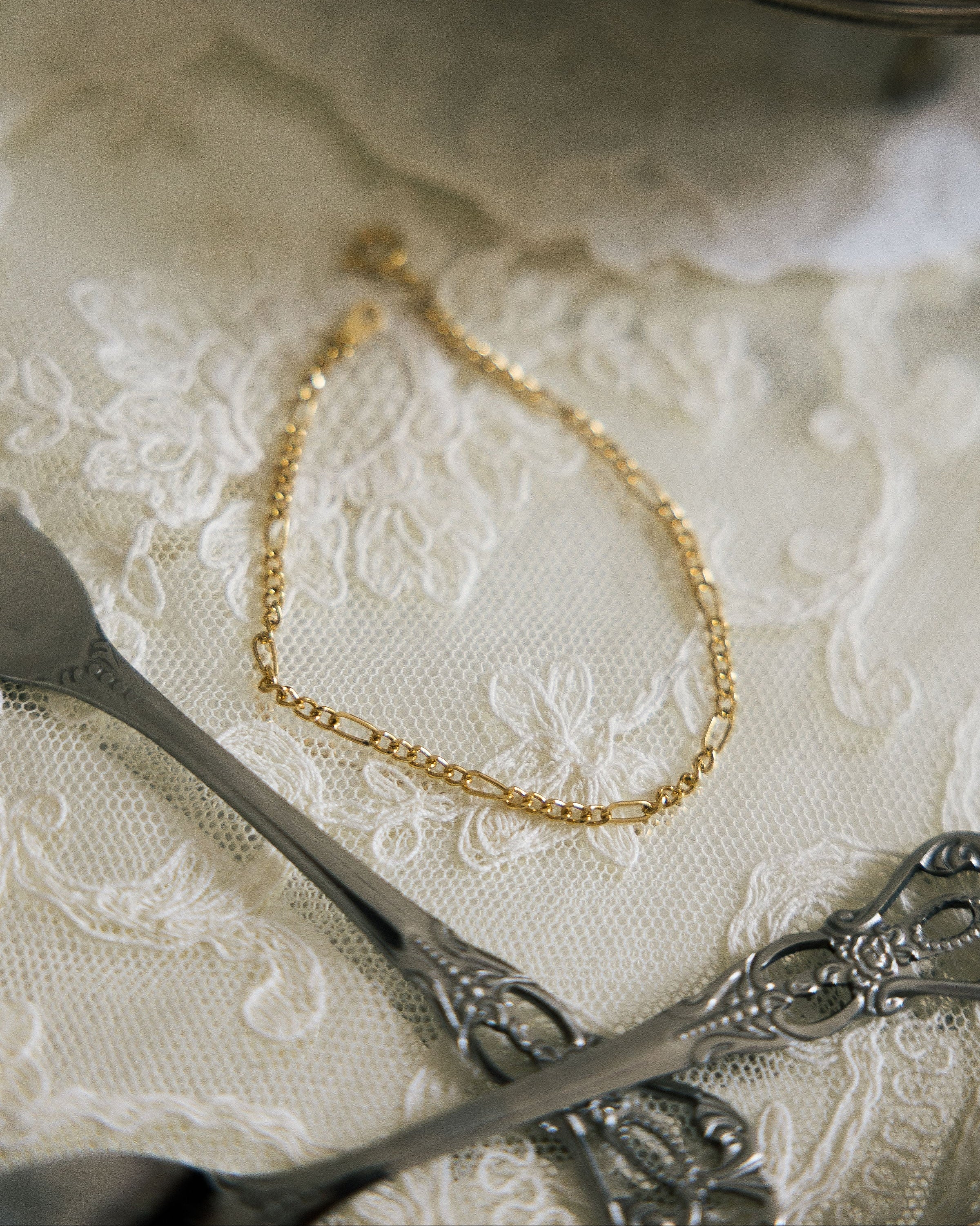 Minimalist Gold Chain Bracelet flat lay on white lace cloth with vintage silver scissors