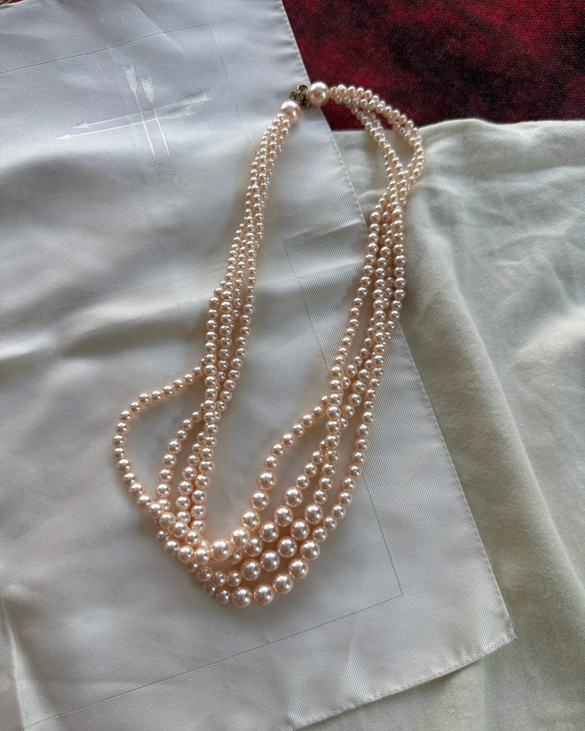 A multi-strand pearl necklace with a silver clasp, draped over a white satin fabric.