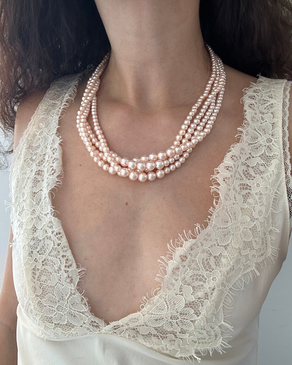 A close-up of a model wearing a multi-strand pearl necklace with a cream lace top.