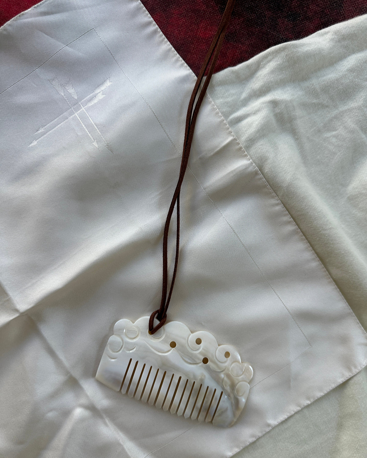 A carved white hair comb with carved details and a brown cord, laid on a white fabric background.