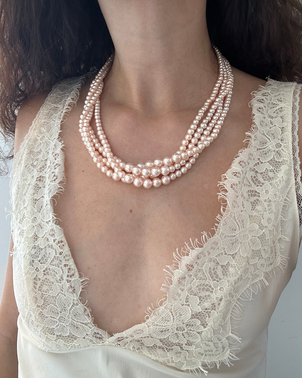 A close-up of a model wearing a multi-strand pearl necklace with a cream lace top.