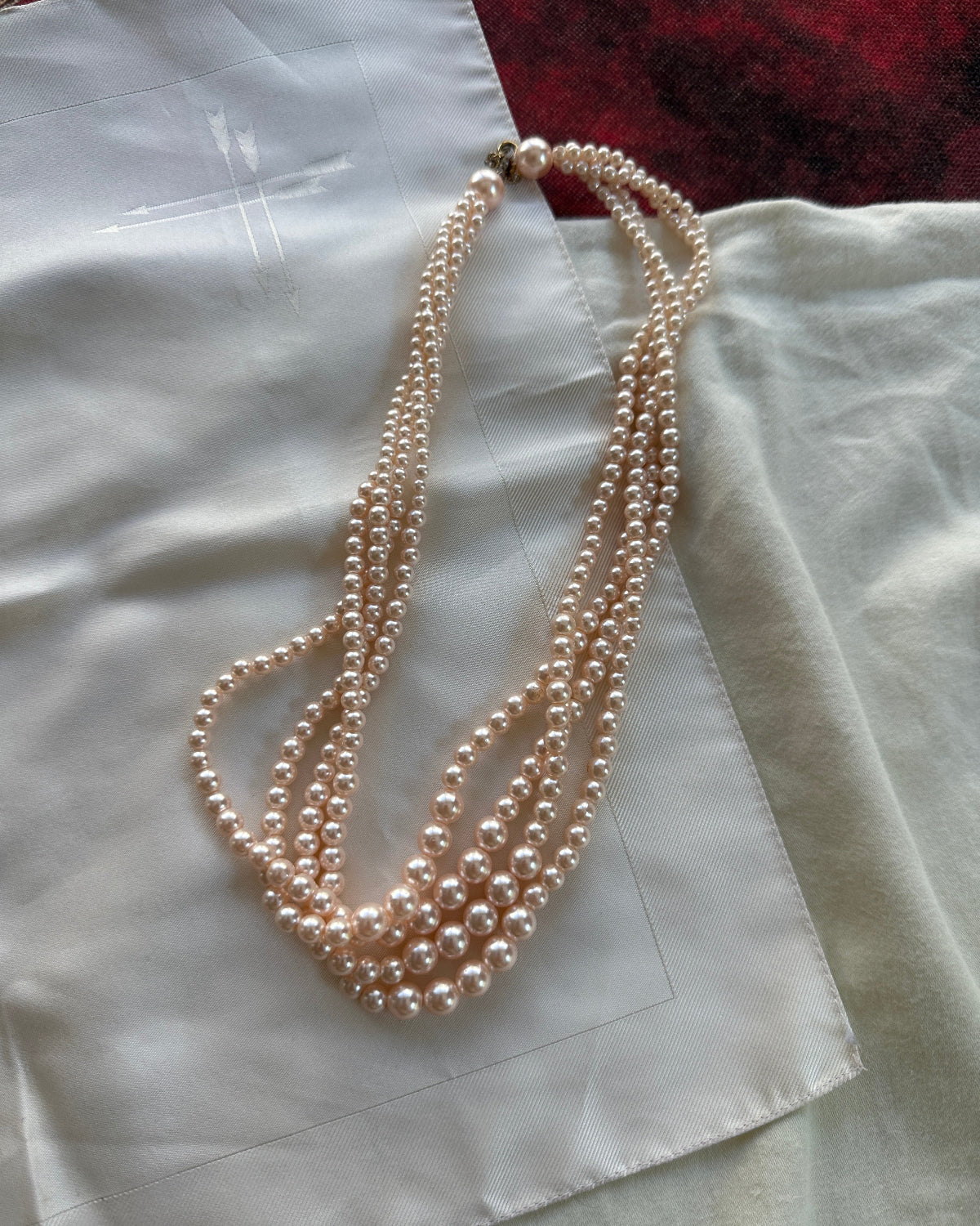 A multi-strand pearl necklace with a silver clasp, draped over a white satin fabric.