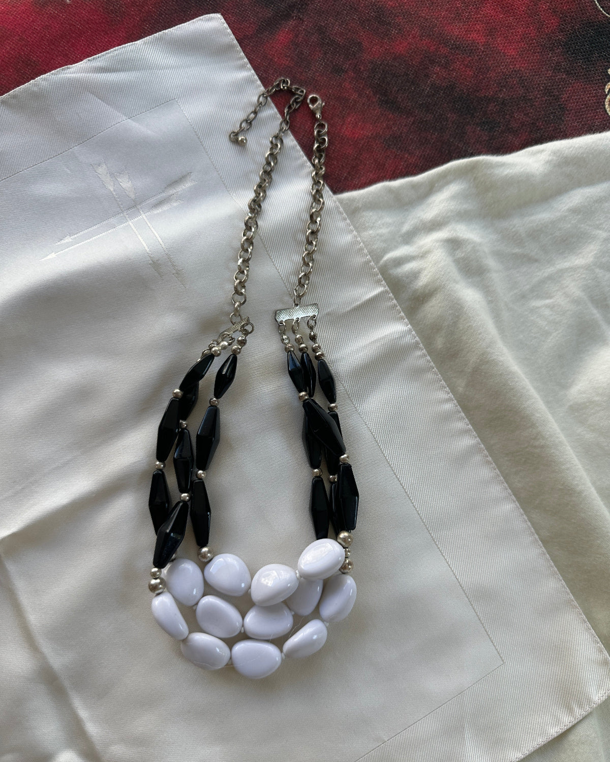 A statement necklace featuring black faceted beads on a silver chain, paired with a large white faux-stone bib collar, laid flat on a cream-colored satin fabric.